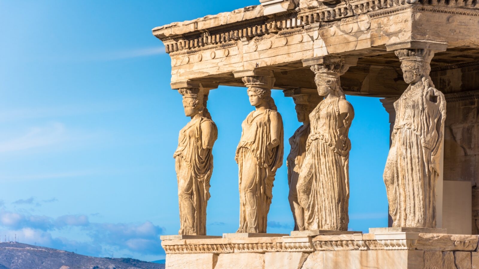 Caryatid statues supporting an ancient Greek temple entablature against a clear sky.