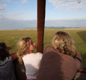 Three people looking out over a savanna from a hot air balloon basket.