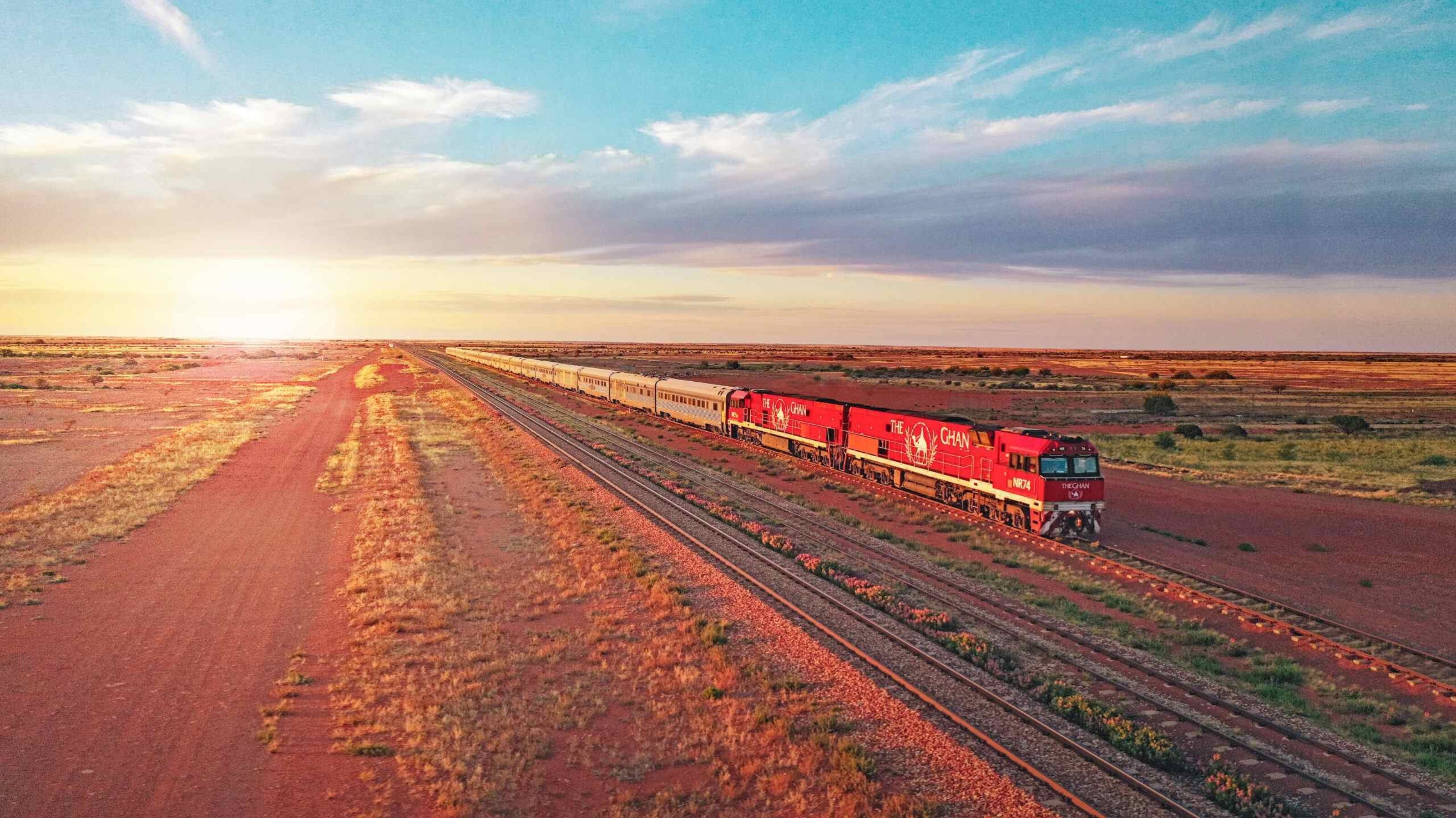 A train crosses a vast desert at sunset, with warm light casting long shadows.