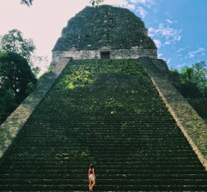 Person ascending ancient Mayan pyramid steps surrounded by lush greenery.