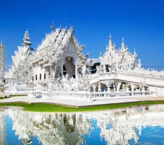 The ornate White Temple in Chiang Rai reflected in a pond with fish.