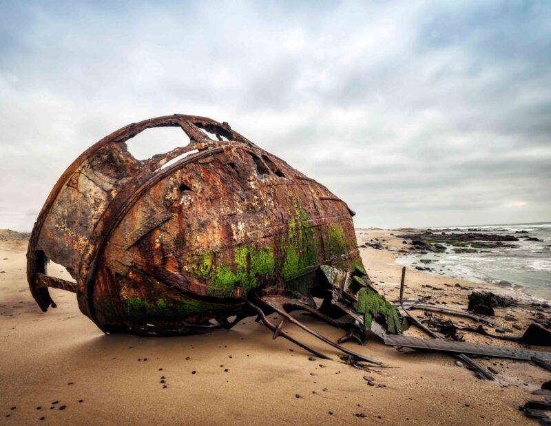 A large, rusted boat wreck sitting on a sandy beach near the ocean waves during Namibia family tours.