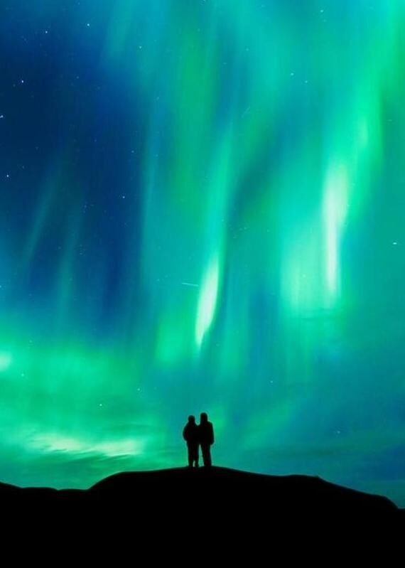 A silhouette of a couple stood watching the northern lights