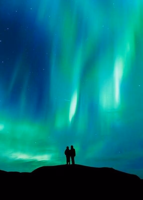 A silhouette of a couple stood watching the northern lights