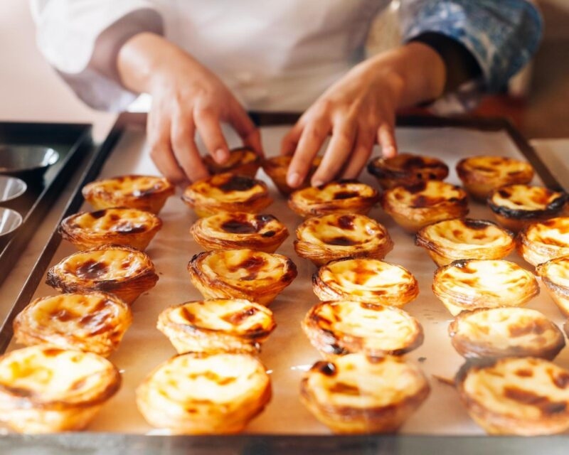 A woman's hands arranging a tray of pasteis de nata in Portugal
