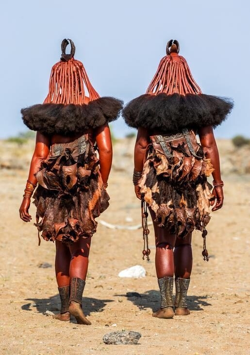 View of the back of two women of the Himba tribe walking in the desert.