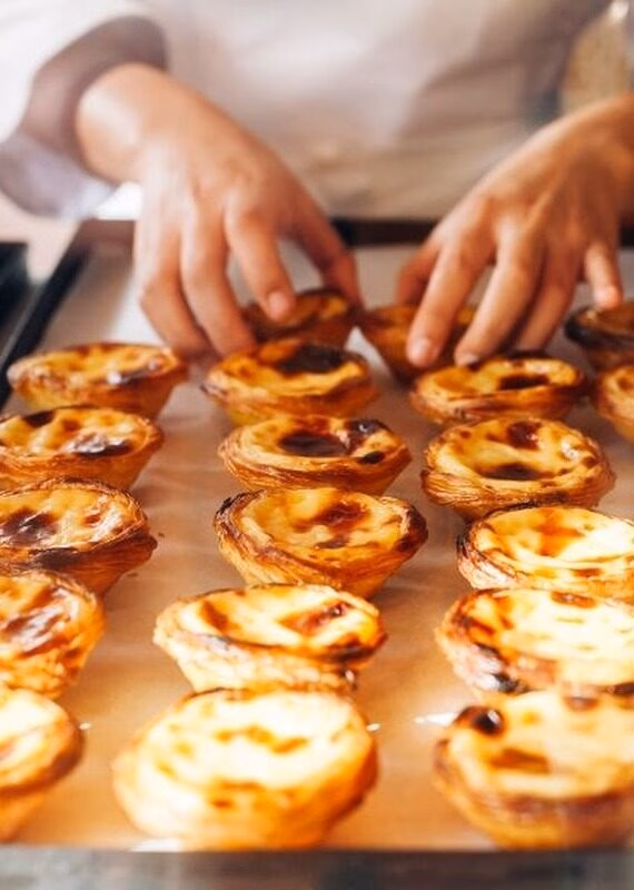 A person in a white chef's coat arranges a tray of freshly baked custard tarts with caramelized tops.