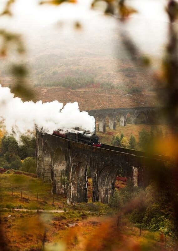Steam train passing Glenfinnan Viaduct with fog covered mountains