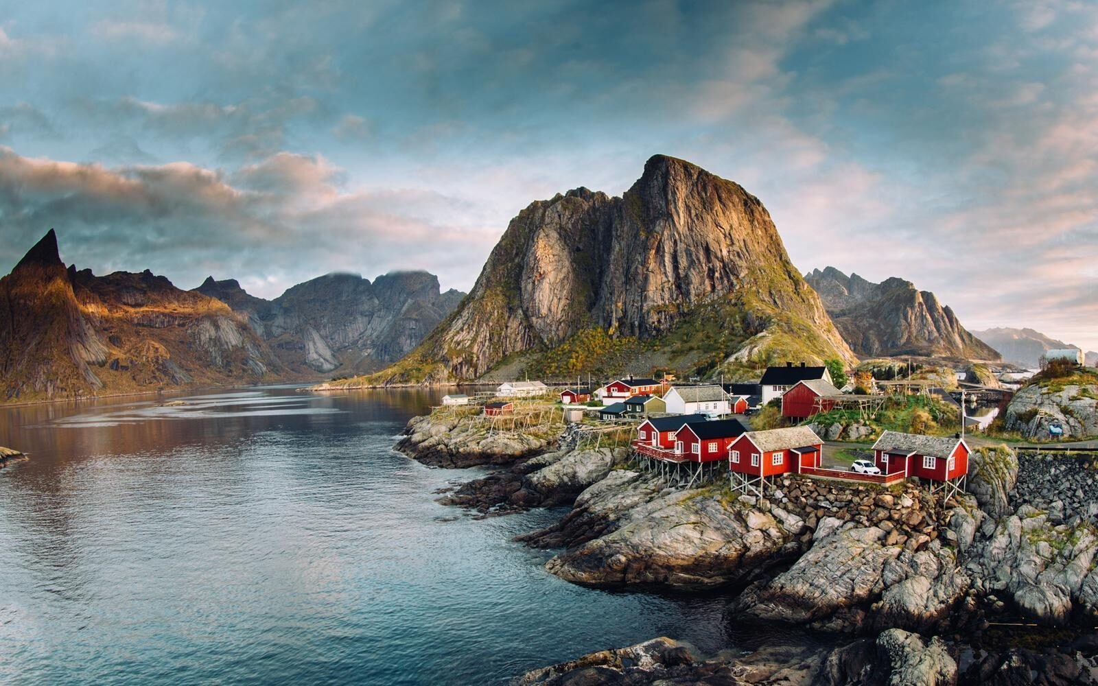 Evening light over the red fishing cabins of the Lofoten Islands with rugged peaks rising above the fjord in northern Norway.