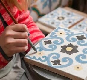 A pottery decorator painting a ceramic tile with floral motifs in his work table in Caltagirone, Sicily is one of our best places to visit in 2026