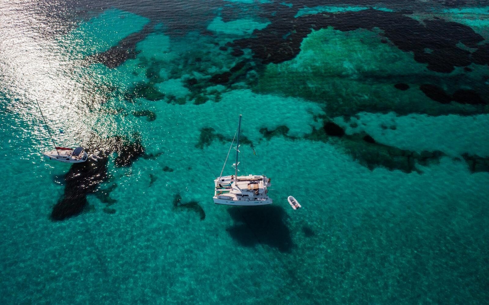 Clear turquoise waters and wildlife-rich reef systems in the Seychelles, where private yachts appear suspended in the air