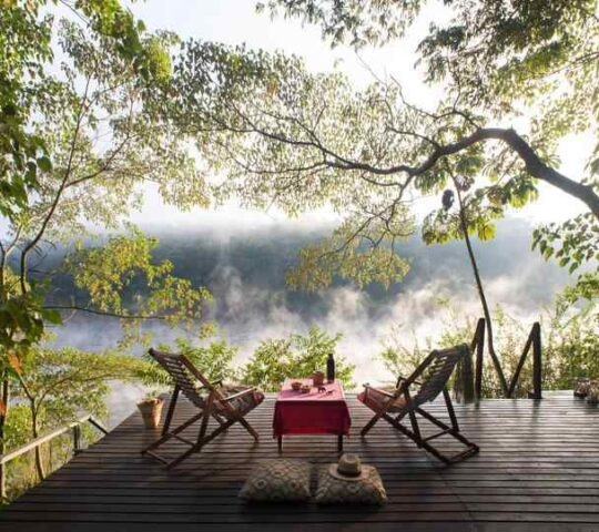 Two chairs on an outdoor deck overlooking a mist-shrouded river.