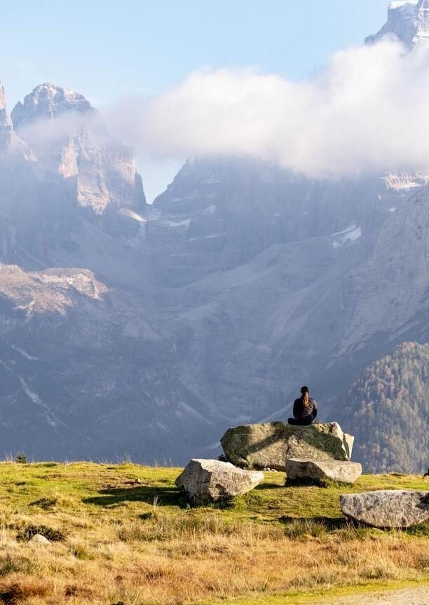 A person meditating on a rock in front of misty, jagged mountains for a positive impact.