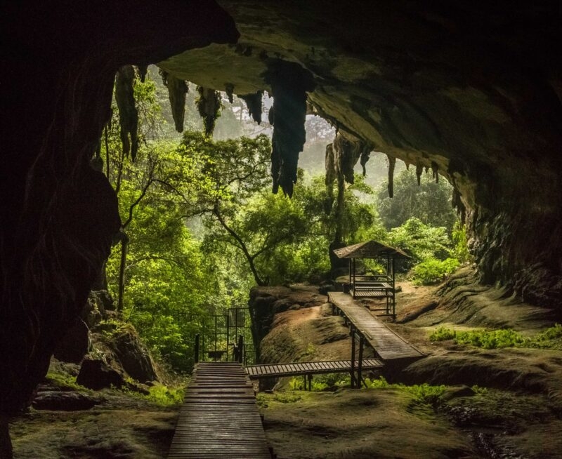 Wooden walkway and small hut inside a dark cave overlooking a bright green jungle on luxury Borneo tours.