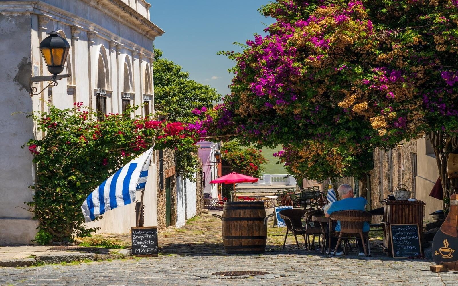 The historic city of Colonia del Sacramento, Uruguay, where some cafés are draped in vibrant bougainvillea blossoms along a cobbled street.