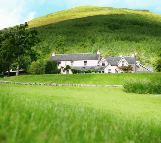 Wide view of a green grassy field with a large pink building in the background and a mountain behind it
