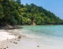 A white sand beach on Gaya Island in Borneo where foliage-cloaked cliffs slope down to the sea.