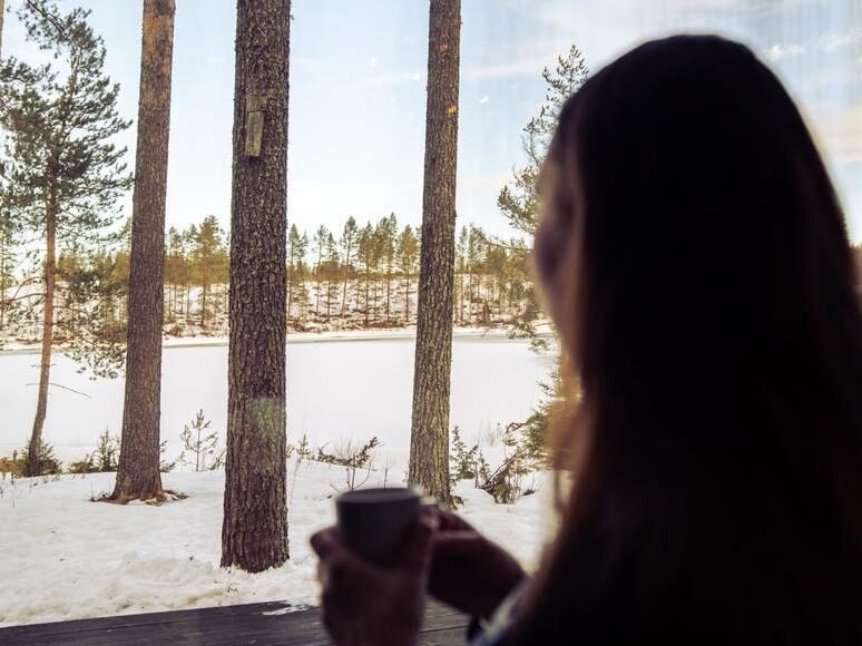 Woman looks out on snowy landscape in her luxury cabin in northern Sweden luxury trip