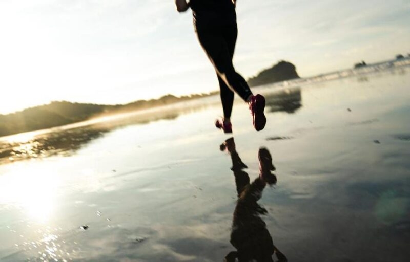 Woman running on an empty beach during sunrise as the light glows on the horizon