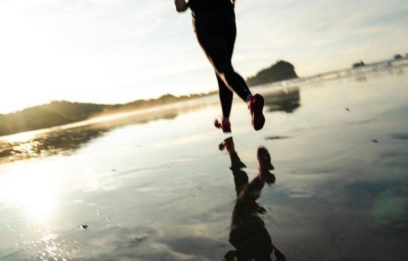 Woman running on an empty beach during sunrise as the light glows on the horizon