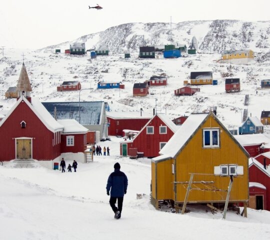 People walking among houses in the Inuit town of Ittoqqortoormiit in Greenland