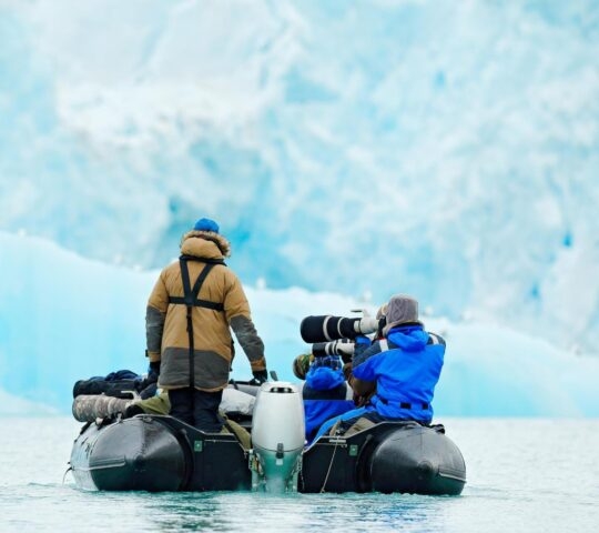 Two people in a zodiac boat with a camera to photograph icebergs in the Arctic