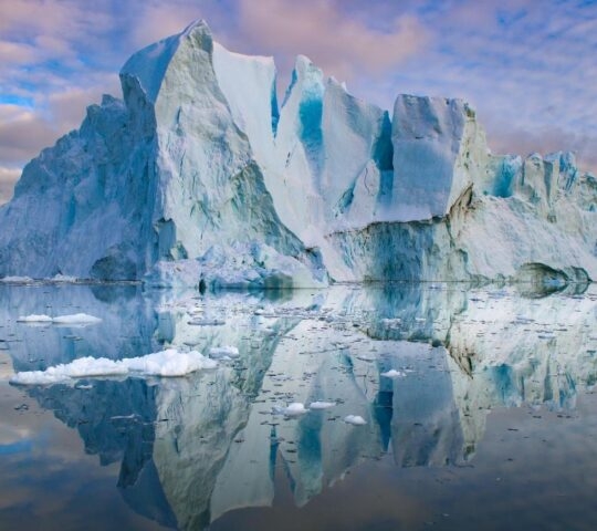 An iceberg reflected in still water at sunset