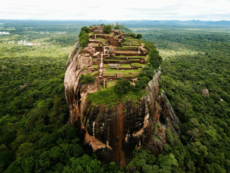 The ancient Sigiriya Rock fortress, a UNESCO World Heritage site in Sri Lanka, towering over lush tropical jungles under a clear sky.