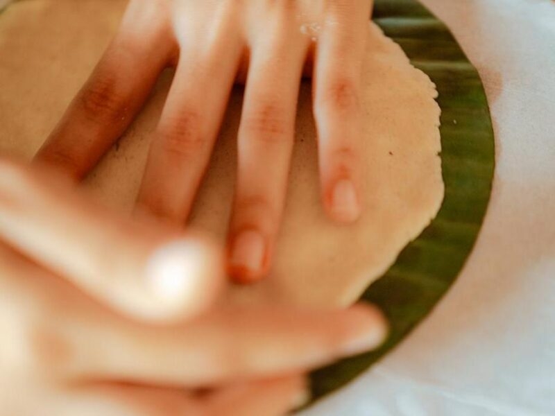 A close-up of hands flattening dough onto a circular green leaf during luxury Family vacations.