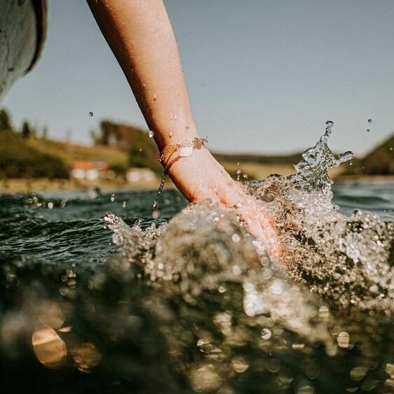 woman on boat is holding hand in water with splashing waves