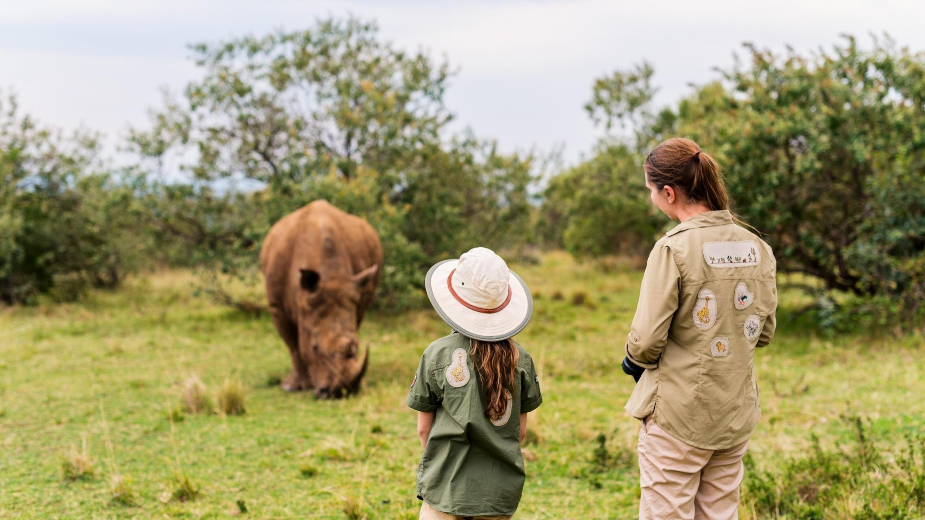 A girl and her mother observing a rhino in the wild.