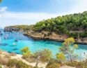 View of a bay with boats floating in turquoise water, surrounded by rocks and trees in Mallorca, Spain