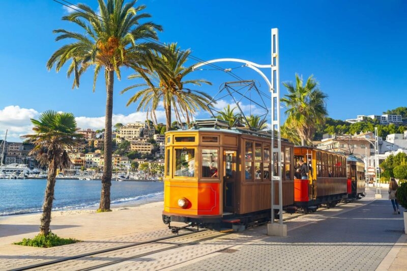 An orange tram travelling past the seafront in Mallorca