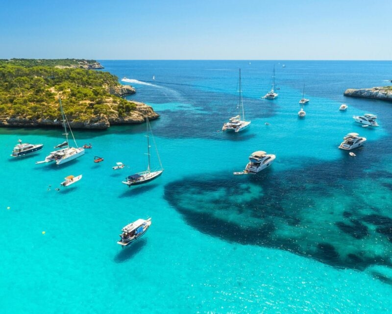 Aerial view of boats floating on bright turquoise water in a bay in Mallorca