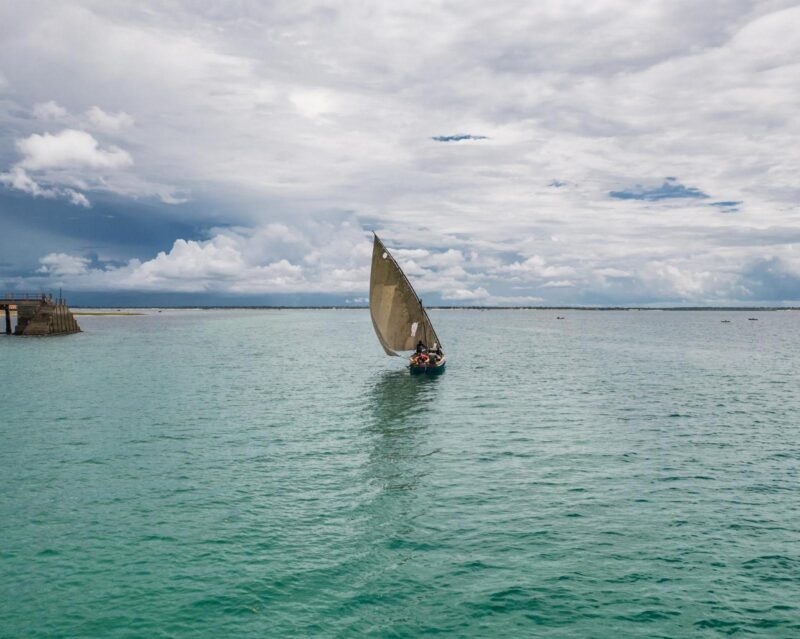 A traditional wooden dhow boat sailing on a calm turquoise sea under a cloudy sky in Mozambique.