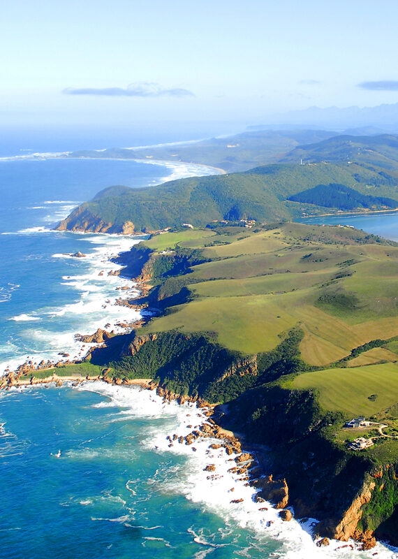 High-angle aerial view of a winding coastline with green cliffs meeting the deep blue ocean and white foam.