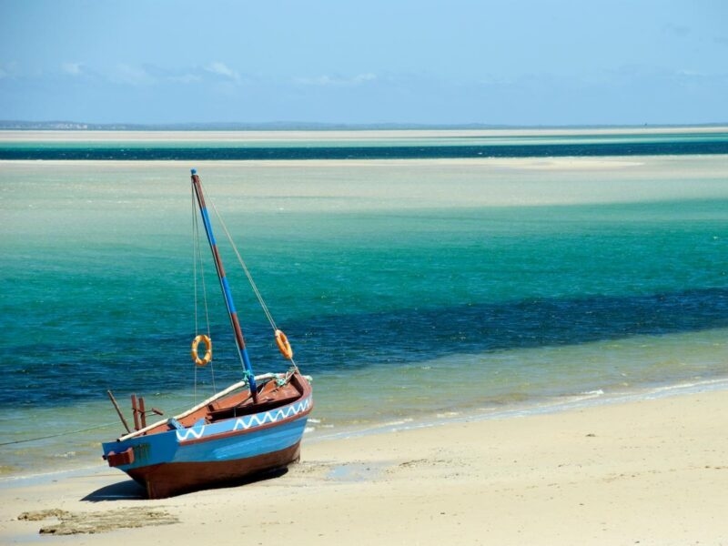 A colorful traditional wooden boat parked on a white sand beach near turquoise ocean water.