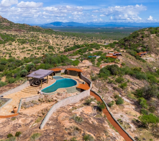 High angle view of a swimming pool and luxury lodge buildings nestled in the rocky landscape of Saruni Samburu.