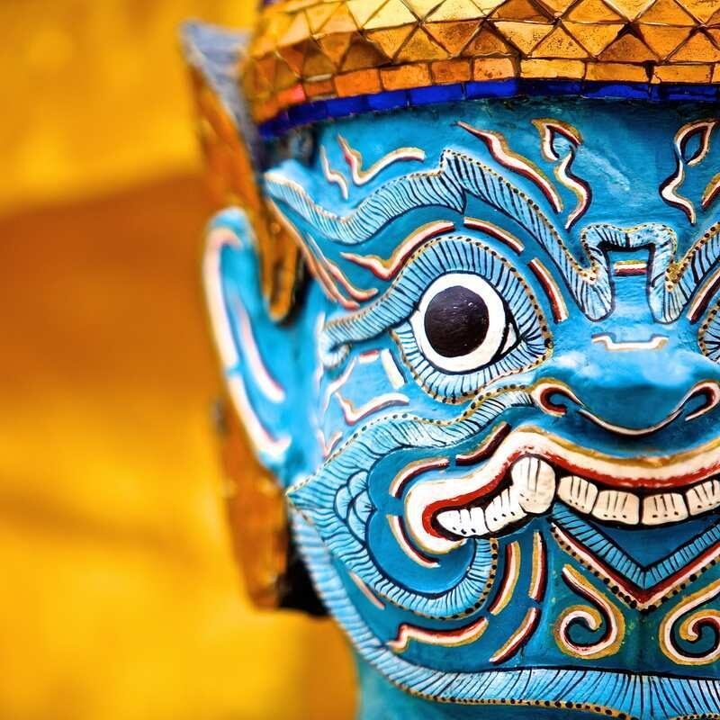 Detailed close-up of a blue-faced guardian statue with wide eyes and white teeth at Wat Phra Kaew.