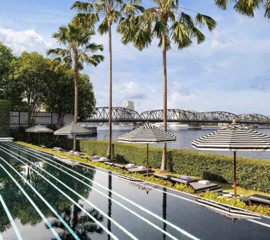 Black tiled infinity pool with white stripes overlooking a river and bridge at the Siam in Bangkok.