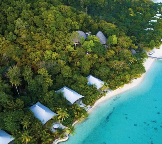 Aerial view of luxury beach suites on a tropical island with turquoise water and dense forest at Bawah Reserve.