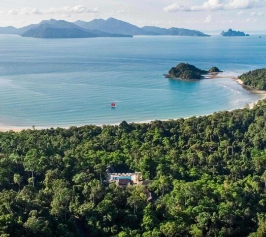 Aerial shot of the Datai in the jungle overlooking a wide bay with a sailboat.