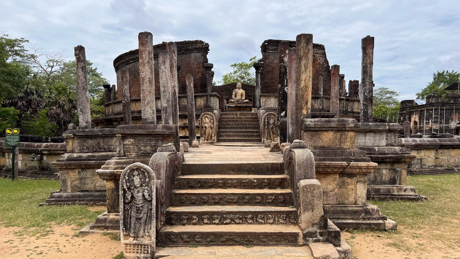 Ancient circular stone temple with pillars and a staircase leading to a seated Buddha statue.