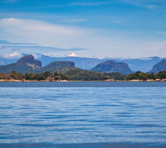 Blue lake water in the foreground with unique rocky peaks and forested islands under a blue sky.