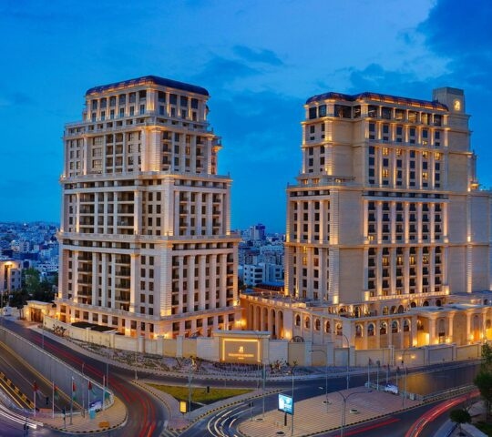 Two grand, lit-up luxury hotel towers at night overlooking the city streets and skyline of Amman, Jordan.