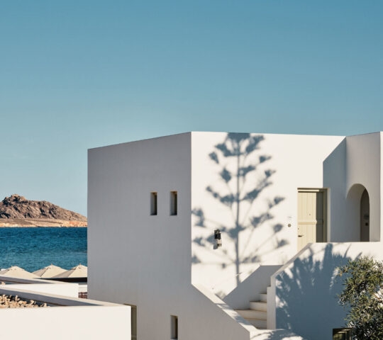A white square building with blue sky and the sea in the background at Cosme, Paros