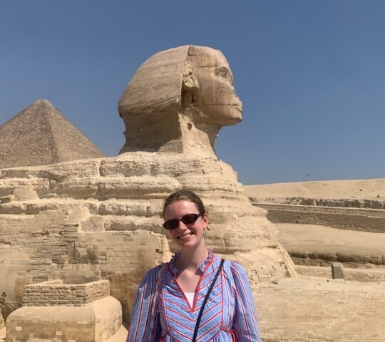 A traveler posing in front of the Great Sphinx and a massive stone pyramid in the Giza desert.