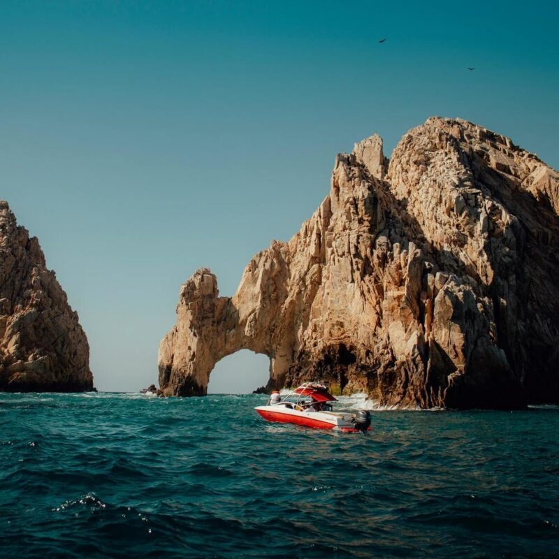 A red boat sails near the El Arco rock formation in Cabo San Lucas, Mexico.