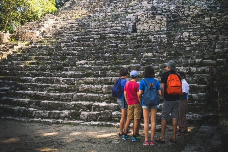 A group of travelers stands before ancient stone ruins while on a Mexico family vacation.