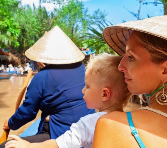 A woman and young boy on a boat ride through a lush Vietnamese waterway with a rower in a conical hat.